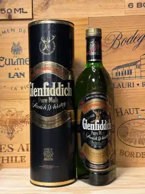 Vintage fles Glenfiddich Pure Malt Scotch Whisky uit de jaren '70 of '80, in iconische driehoekige fles met donkergroen glas, groen gouden label met hertensymbool en rode accenten, gepresenteerd in een kartonnen koker.
