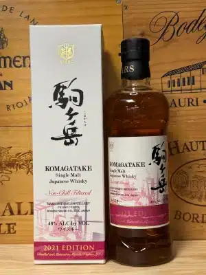 Een fles Mars Komagatake Limited Edition 2021 single malt whisky, met een verfijnd label en heldere amberkleurige inhoud. De fles staat voor een achtergrond van bergen, verwijzend naar de Japanse Alpen nabij de Shinshu-distilleerderij waar de whisky is geproduceerd.