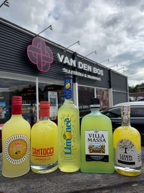 Verse citroenen, een fles limoncello en een glas op een Italiaanse houten tafel – symbool voor ambachtelijke citroenlikeurproductie.